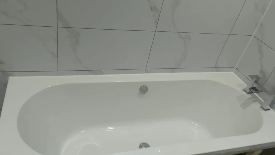 White fitted bath with marble-effect panel and walls